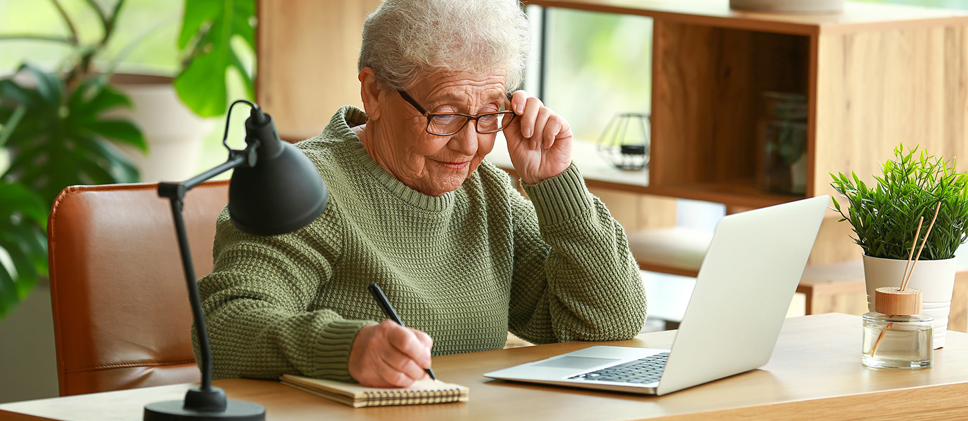 Older woman writing notes from her laptop